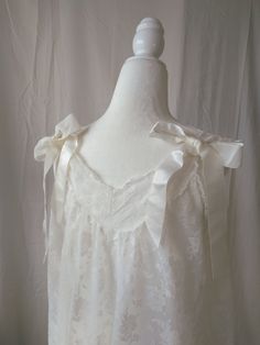 Vintage white lace and ribbon nightgown by Aristocraft. Features sheer lace overlay against nylon lining, standard sleeveless straps decorated with satin bows on the back of the straps, decorative satin ribbon accents placed vertically across the front, and satin bows across the lightly ruffled hem. Straps are not adjustable. Era: Circa 1960s Condition: Excellent Size: Small Color: White Brand: Aristocraft Measurements: 20.5in pit to pit, 38.5in length Fabric Content: 100% nylon Shown on a mannequin with a 33" bust, 26" waist, and 35" hips. Fits a size 2-4. Model is 5'5 with a 34A bust. Some garments may be clipped onto mannequin or model for display. MORE INFO: *Please, note that these items are vintage. Therefore, it is expected to find some wear. Ariessence by Ariel is an admirer of fas Cream Lace Wedding Nightgown, Wedding Cream Lace Nightgown, Cream Lace-trim Sleepwear For Wedding, Vintage Wedding Nightgown With Delicate Lace, White Delicate Lace Trim Nightgown, Delicate White Nightgown With Lace Trim, Cream Wedding Sleepwear With Lace Trim, White Lace Nightgown For Wedding, White Lace Wedding Nightgown