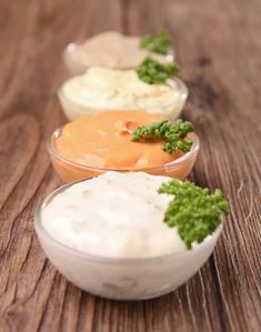 three small bowls filled with different types of dips on a wooden table, one is topped with parsley