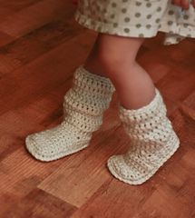 a close up of a child's feet wearing crocheted boots on a wooden floor