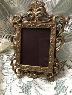 an ornate gold frame sitting on top of a lace covered tablecloth with a white flower