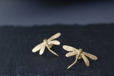 two small gold dragonflys sitting on top of a black piece of cloth next to each other