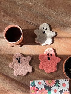 three little ghost coasters sitting next to a cup of coffee on a wooden table