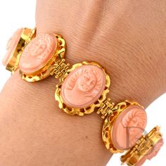 This delicate and intricate vintage coral bracelet was crafted in 18K yellow gold. Featuring 8 carved coral Cameos bezel set, each measuring appx. 14.50mm x 19.50mm. Each cameo face is unique and all are hinged between and set in an intricately carved link. Measuring appx. 24.38mm x 7.25 Inch, this soft pinkish colored coral cameo bracelet will enhance any attire. Stamped with purity mark. Remains in Excellent Condition. Accompanied by a professional appraisal document. Luxury Round Coral Jewelry, Luxury Coral Jewelry For Formal Occasions, Formal Coral Oval Jewelry, Formal Coral Jewelry With Cabochon Details, Formal Coral Jewelry With Cabochon, Orange Bracelet For Formal Occasions, Formal Orange Bracelet Jewelry, Formal Orange Bracelet, Luxury Carved Bracelets For Formal Occasions