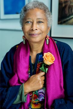 an older woman holding a rose in her right hand and wearing a purple scarf around her neck