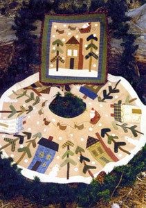 a quilted table cloth with houses and trees on it, sitting in the grass