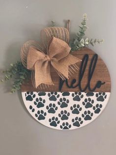 a wooden sign that says hello with paw prints and a bow on it's front