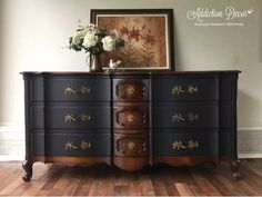 an ornate dresser with flowers on top in front of a painting and wooden flooring