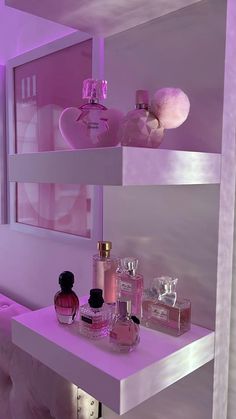 two shelves with perfume bottles on them in a pink lit room next to a bed