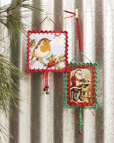 two christmas ornaments hanging from a string on a wall next to a pine tree and tin foil