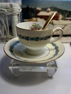 a cup and saucer sitting on top of a glass stand with a spoon in it