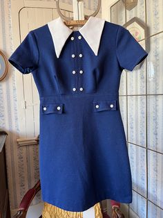 This cute dress comes from Wendy Lane, Montreal. It's made from fortrel in dark royal blue with a pointy wide fortrel collar and little white buttons down the front and on the faux pockets. It fastens with a long zipper in the back. The measurements, taken with the dress lying flat, are: shoulder to shoulder, 14 inches; armpit to armpit, 16 inches; sleeves, 7 inches; waist, 13 inches; length, 30 inches; bottom edge, 21 inches. In good condition. Preppy Fitted Mini Dress, Preppy Fitted Knee-length Dresses, Fitted Blue Dress With Doll Collar, Fitted Collared Short Sleeve Dress, Blue Short Sleeve Dresses With Buttons, Preppy Fitted Collared Dress, Fitted Preppy Mini Dress, Vintage Fitted Mini Dress With Doll Collar, Vintage Blue Dress With Doll Collar