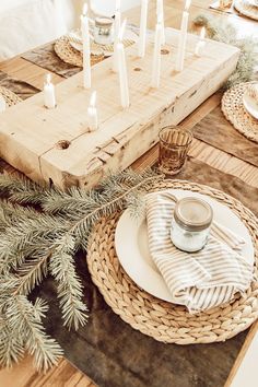 the table is set with candles and dishes on it, along with pine branches in wicker baskets