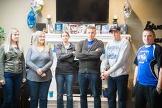 a group of young people standing in front of a tv screen with their arms crossed