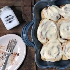 a blue dish filled with cinnamon rolls next to a plate of cake and a jar of milk