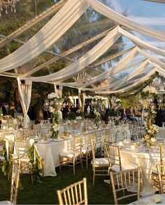 an outdoor wedding reception setup with white linens and gold chairs, chandeliers and greenery