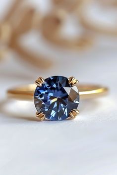 a blue diamond ring sitting on top of a white surface with gold trimmings