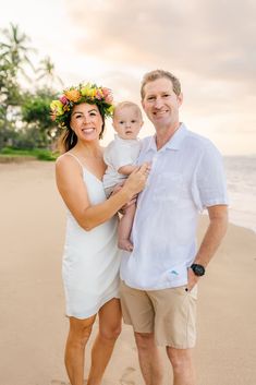 a man and woman holding a baby on the beach