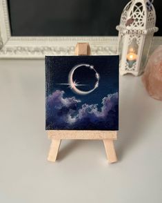 an easel with a painting on it sitting next to a candle and a mirror