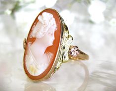 Exquisite vintage cameo ring beautifully crafted of 10K tri-colored gold with a rose gold orange blossom and green colored gold accents on each east/west side of the shell cameo! This elongated oval shaped cameo ring is  bezel set in yellow gold and is so pretty and feminine! It portrays an anonymous woman with what looks to be either wavy shorter hair or in a chignon facing to the right and the workmanship of the cameo details including the floral orange blossom details of this Esemco hallmarke Etsy Engagement Rings Unique, Elongated Oval, Shorter Hair, Unique Engagement Ring, Cameo Ring, Vintage Cameo, West Side, Gold Orange, Unique Engagement