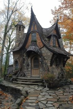 a house made out of rocks and trees with leaves on the ground next to it