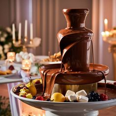 a chocolate fountain with fruit and marshmallows on the bottom is surrounded by candles