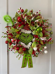 a christmas wreath hanging on the front door with green and red decorations around it, including an elf's head