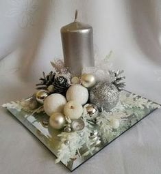 a candle and some ornaments on a glass plate with snowflakes, pine cones and silver balls