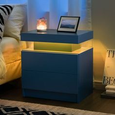 a blue night stand with a lit candle on it next to a bed and pillows