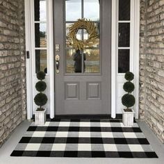 the front door is decorated with black and white checkered rugs, potted boxwood trees, and a wreath