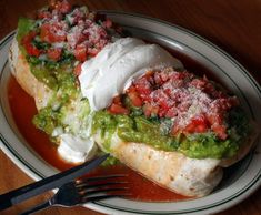 two burritos on a plate with salsa and sour cream, sitting next to a fork