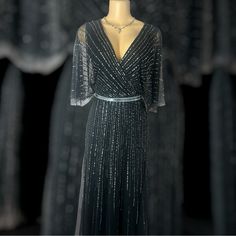 This Is A Sophisticated Black Evening Gown Adorned With Shimmering Sequin Stripes That Create A Radiant, Starburst Effect. The Flowy, Sheer Cape Sleeves Add A Graceful Touch, While The Metallic Belt Cinches The Waist For A Flattering Silhouette. Perfect For Formal Occasions Or Elegant Parties. Elegant Gray V-neck Evening Dress, Black Evening Mother Of The Bride Dress, Fitted Floor-length Black Mother Of The Bride Dress, Elegant Black Floor-length Mother Of The Bride Dress, Elegant Gray Evening Dresses, Black Floor-length Mother Of The Bride Dress, Elegant Black Mother Of The Bride Evening Dress, Black V-neck Gown For Evening, Gray Fitted Evening Dress For Mother Of The Bride