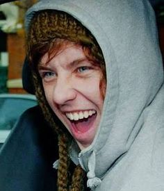 a man in a gray hoodie is smiling and wearing a knitted hat with dreadlocks