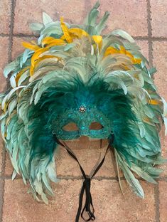 This large gorgeous Mardi Gras mask is turquoise blue iridescent lace and glitter face with turquoise feathers accented by gold yellow and white. Hand painted hand feathered headdress.  Large feathered mask made by New Orleans premier maskmaker. Made by hand by local French Quarter artist for Mardi Gras parades, balls, masquerades, or your occasion. Our masks also come ready to display on your wall or mask stand.  Lightweight and comfortable. Beautiful jewel in center of forehead.  This beautiful one of a kind mask would look stunning on men or women for your event.  We do custom work and would love to talk to you about your wedding or birthday or masquerade. 20 years experience making masks for all sorts of special occasions. We can even make changes to the masks currently for sale. Messa Mardi Gras Feathers, Feathered Mask, Feathered Headdress, Dance Decor, Dance Decorations, Mardi Gras Outfits, Mardi Gras Parade, New Orleans Mardi Gras, Glitter Face