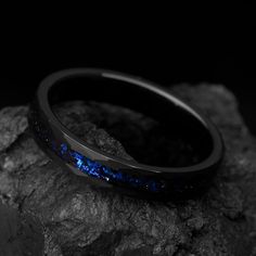 a black and blue ring sitting on top of a rock in front of a dark background