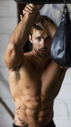 a shirtless man holding a black bag over his head while standing next to a punching bag