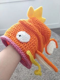 a hand is holding a crocheted orange and white hat with a fish on it