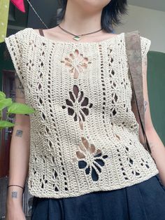 a woman wearing a crochet top with flowers on the front and back, standing next to a plant