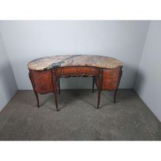 an old wooden desk with marble top and drawers on the bottom, against a white wall