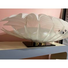 a large white flower shaped glass bowl sitting on top of a wooden table next to a pink wall