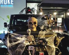 two skeletons in front of a truck with spider webs on the hood and hands