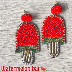 two red and green beaded earrings with watermelon on them, sitting on a wooden surface