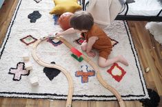 a toddler playing with a toy train set on the floor next to a rug