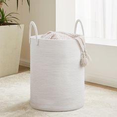 a large white basket sitting on top of a rug next to a potted plant