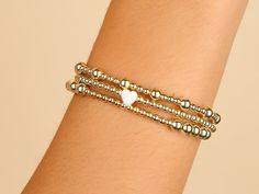 Dainty and enchanting, this 3mm bead bracelet with a Mother of Pearl heart charm is a symphony of subtle elegance. The golden beads offer a warm glow, while the heart charm brings a meaningful whisper of love and tenderness to the wrist. Ideal for layering or wearing solo, it's a versatile token of affection that's as timeless as it is trendy.﻿ 14K gold filled. Bead size: 3mm. Mother of Pearl Heart Charm: 6.5 x 7mm. 6.75 inch strong stretchy elastic band. Hypoallergenic, waterproof and tarnish r Dainty Heart Charm Bracelet With Round Beads, Everyday Heart-shaped Jewelry With Tiny Beads, Dainty Bracelet With Heart Charm And Round Beads, Elegant Beaded Bracelet With Heart Charm For Valentine's Day, Elegant Beaded Heart Charm Bracelet, Elegant Beaded Bracelet With Heart Charm For Wedding, Elegant Heart-shaped Beaded Charm Bracelet, Elegant Wedding Beaded Bracelet With Heart Charm, Everyday Heart Bracelet With Round Beads