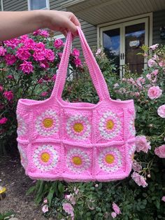 a pink crocheted purse with yellow and white flowers in front of some bushes