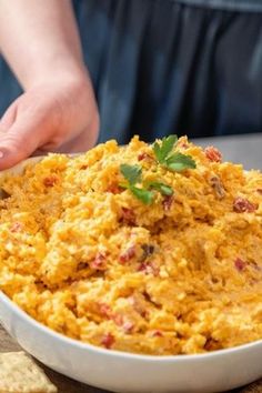 a person holding a spoon in a white bowl filled with mashed potatoes and garnished with parsley