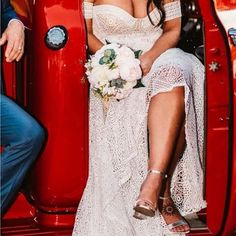 a woman sitting in the back of a red truck wearing a white dress and holding a bouquet