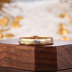 a gold wedding band with blue stones sits on top of a wooden box