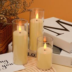 three lit candles sitting on top of a table next to books and a vase filled with flowers