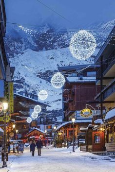 people are walking down the street in front of buildings with christmas lights hanging from them